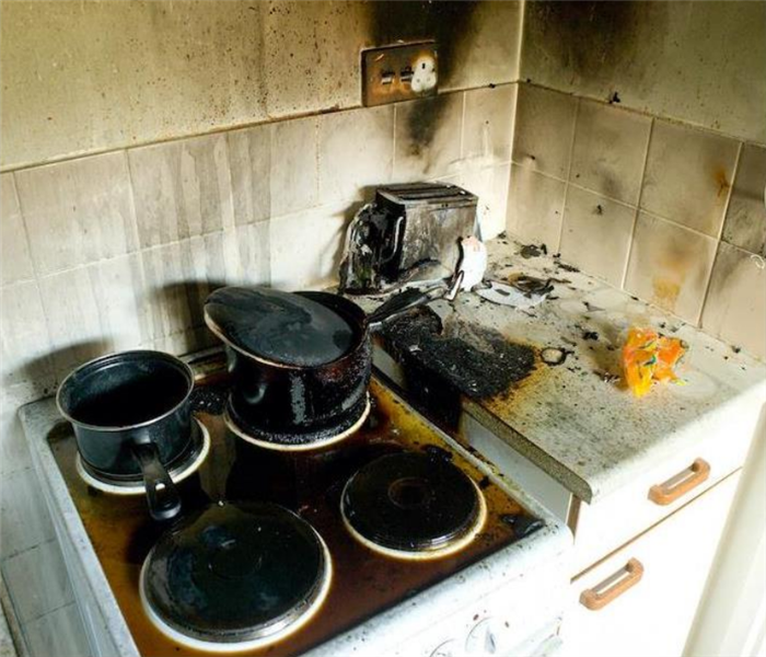 a fire damaged stove in a kitchen with soot covering the walls and pots