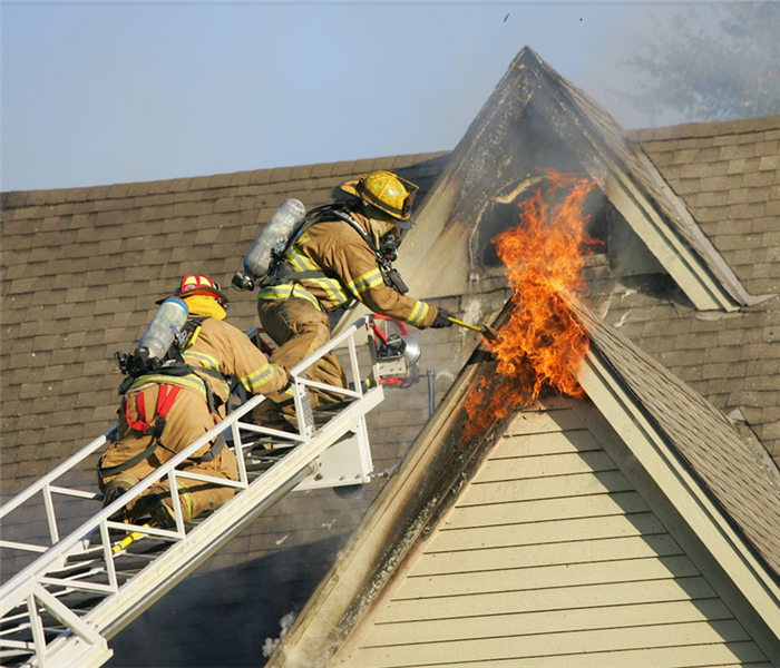a fireman on a ladder putting out a fire in top of a house